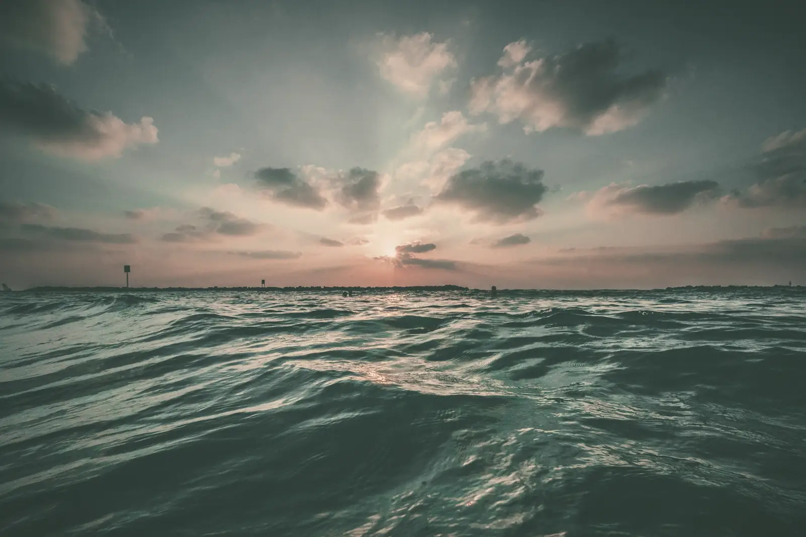 Calm, dark ocean at dusk under low clouds.
